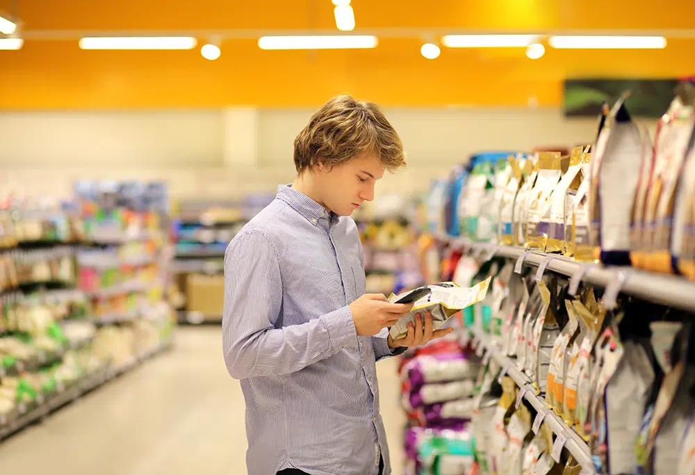 Young man choosing pet food by reading labels in a supermarket aisle — guidance for new pet parents from VNGOO blog